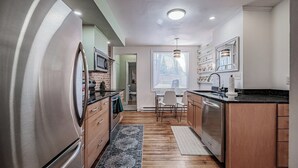 A modern kitchen with stainless steel appliances, wooden cabinets, and a dining area with a table and chairs. - Experience Portland’s charm in this beautifully restored 2-bed, 1.5-bath Victorian apartment! Located downtown, enjoy modern comforts, historic elegance, a private backyard, AC, and 1 free parking spot. Perfect for your Maine getaway! 🦞 (Portland)