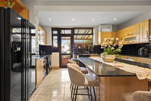 Una cocina moderna con un refrigerador negro, armarios de madera, una isla grande con taburetes de bar y una planta en maceta.