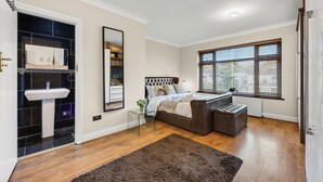 A bedroom with a bed, a bedside table, a window with blinds, a radiator, and a door. - 6 bedroom spacious house minutes from Wembley Stadium (Wembley)