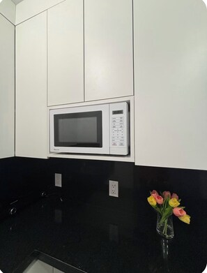 A kitchen with a microwave, black countertop, and a vase with flowers. - Pocket Paradise - Guest suite (Miami)