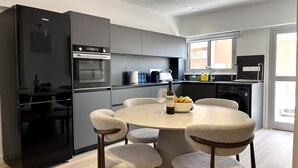 Una cocina moderna con horno empotrado, refrigerador y comedor con mesa redonda y cuatro sillas.