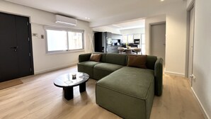 Una sala moderna con un sofá modular, una mesita de centro redonda y una cocina al fondo.