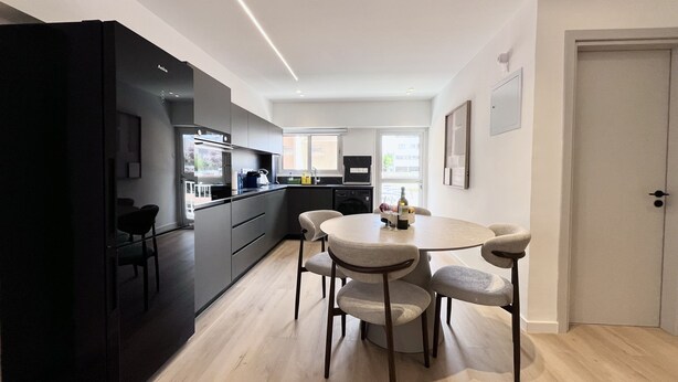 Una cocina moderna con comedor, que incluye un refrigerador negro, una mesa redonda con sillas y una puerta a la derecha.