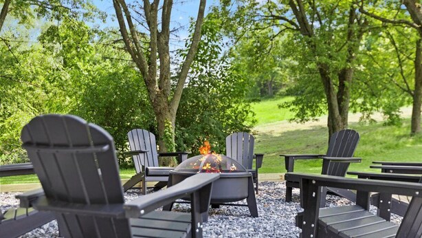 A fire pit with chairs around it, set on gravel, surrounded by trees. - Charming Hudson Farmhouse with Fire Pit (Hudson)