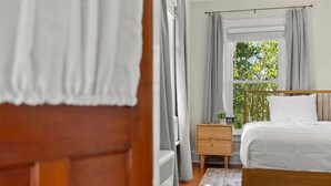 A bedroom with a wooden bed, a nightstand, a window with curtains, and a view of greenery outside. - Charming Hudson Farmhouse with Fire Pit (Hudson)