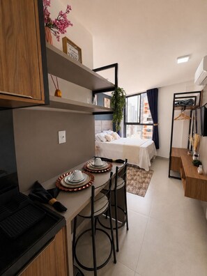 A compact hotel room with a kitchenette, a dining area, a bed with a view, and a small seating area. - Premium Studio with Ocean View in Manaíra. (João Pessoa)