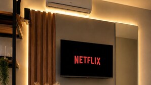 Een moderne woonkamer met een tv aan de muur waarop 'NETFLIX' staat, een houten console met decoratieve objecten, en een airconditioner erboven.