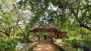 A traditional pavilion with a tiled roof, surrounded by lush greenery and a water feature.