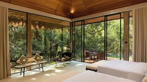 A modern room with large windows, a sofa, a dining table, and a bed.