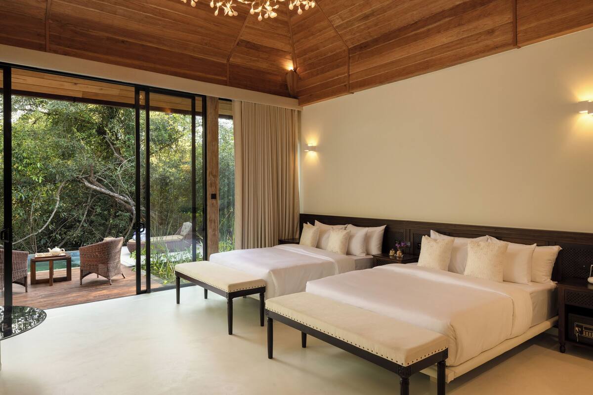 Un dormitorio con dos camas, techo de madera y vistas a una piscina y árboles.