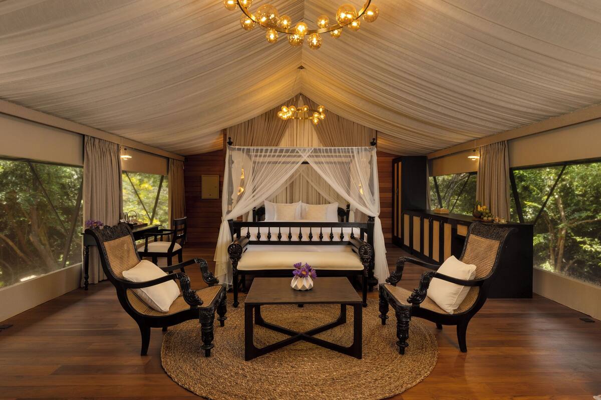 Una habitación tipo tienda con una cama, dos sillas, una mesa y un candelabro.