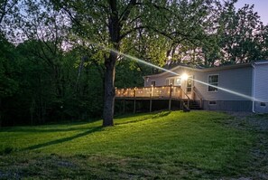 A house with a deck, surrounded by trees and a grassy yard.