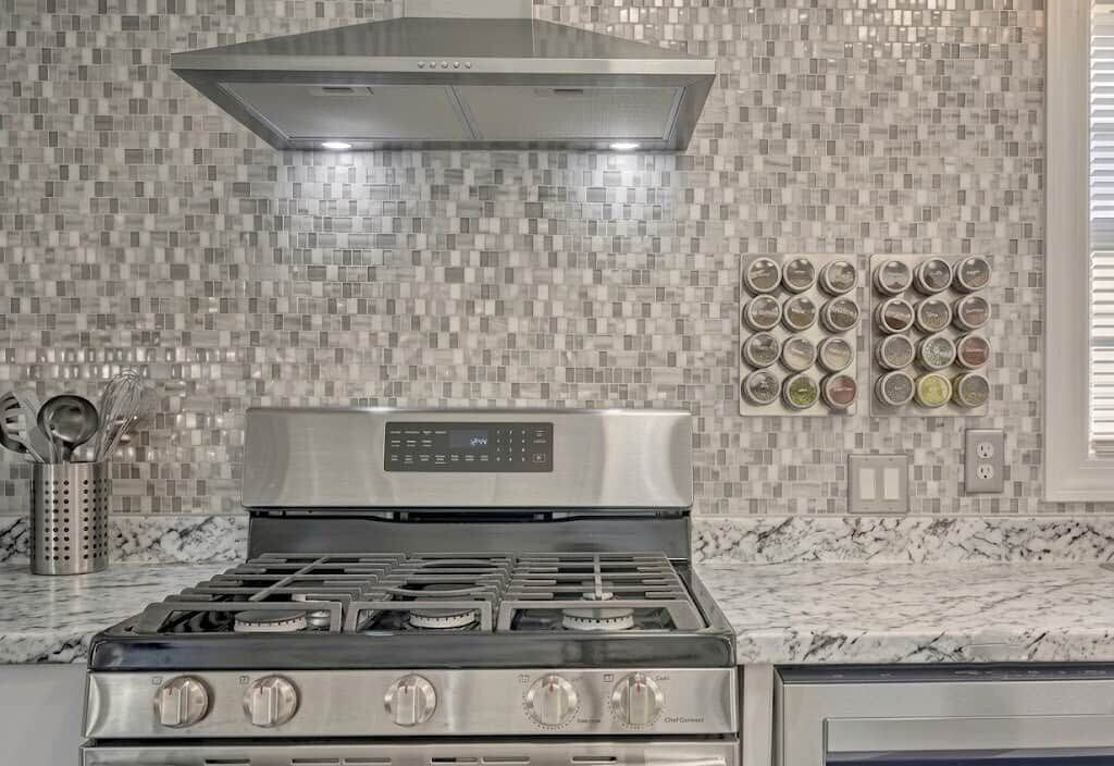 Cozinha com fogão de aço inoxidável, painel de controle digital e backsplash com azulejos quadrados.