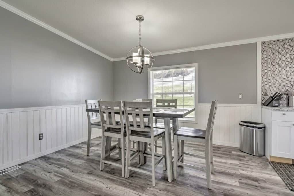 A dining area with a table and chairs, a hanging light fixture, a window with blinds, and a trash can.