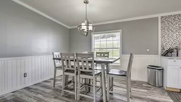 A dining area with a table and chairs, a hanging light fixture, a window with blinds, and a trash can.
