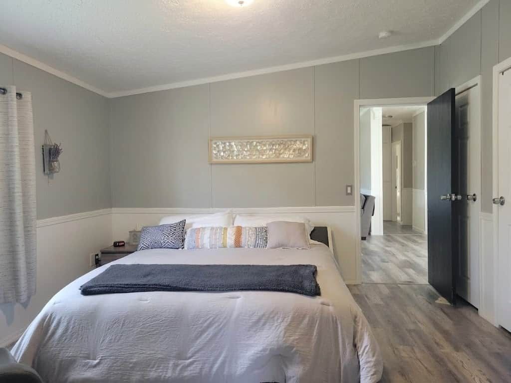Une chambre à coucher comprenant un lit, des tables de chevet, une commode, un luminaire fixé au mur et une porte donnant sur une autre pièce.