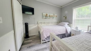 Une chambre avec deux lits, un téléviseur à écran plat fixé au mur, un tableau et une fenêtre avec des stores.