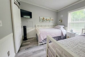 Un dormitorio con dos camas, un televisor de pantalla plana montado en la pared, un cuadro y una ventana con persianas.