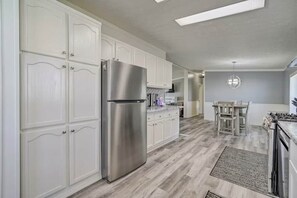 Una cocina moderna con armarios blancos, un refrigerador de acero inoxidable y un comedor con mesa y sillas.