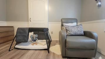 Une pièce avec un parc pour bébé, un fauteuil gris et une porte blanche.