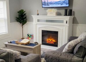 A living room with a fireplace, a television mounted above it, and a plant on the mantel. - Family-Friendly By Fishing, Hiking, and Wine Trail (Seneca Falls)