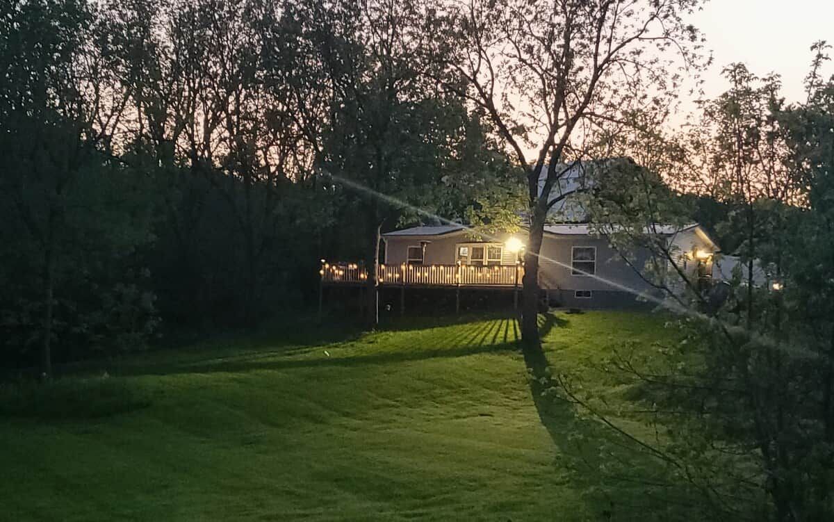 A house with a deck, surrounded by trees and a grassy yard.