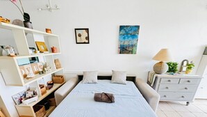 Et soveværelse med seng, sengeborde, kommode, hylder med forskellige genstande og kunst på væggen.