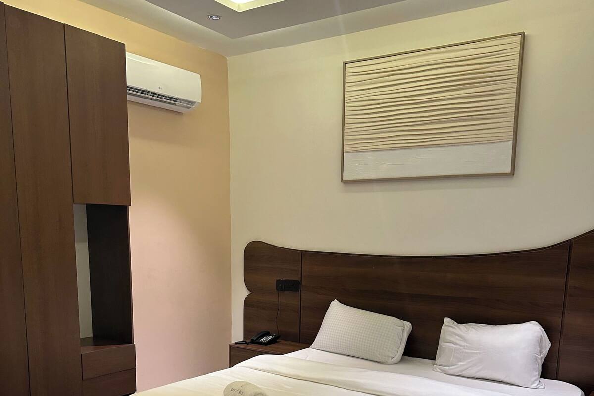 A neatly made bed with white linens, a wooden headboard, and a wall-mounted artwork.