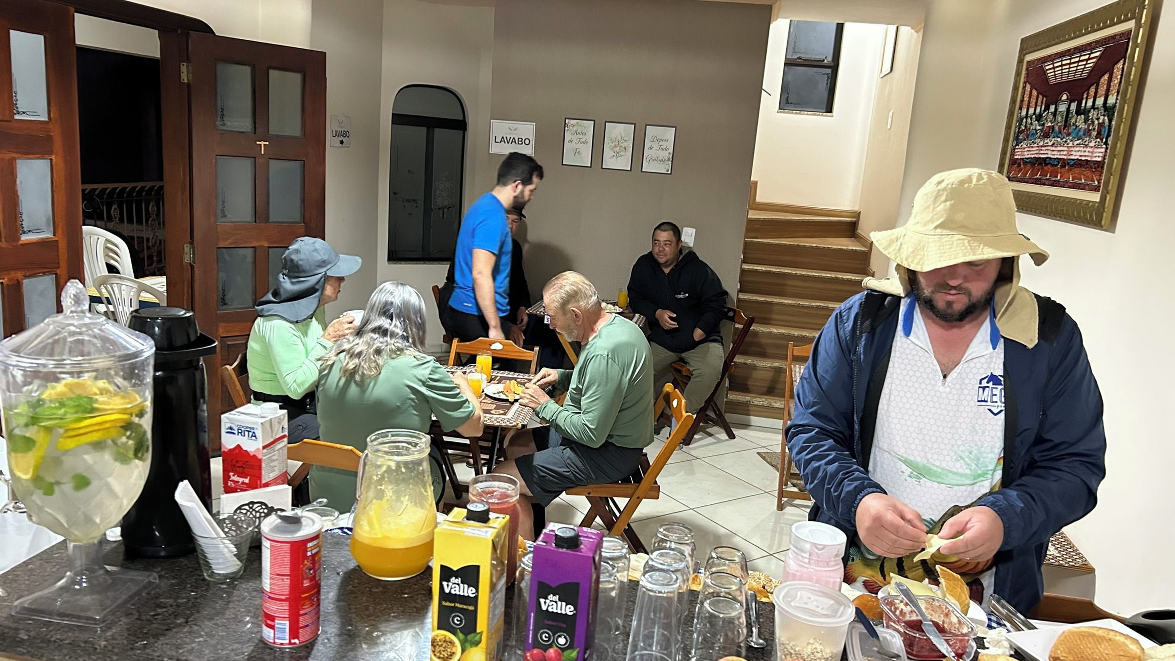 Uma sala de jantar com mesa posta para refeição, uma pessoa preparando comida e uma escada ao fundo.