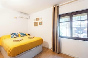 A room with a bed, a window with curtains, an air conditioning unit, and framed pictures on the wall. - Las Rotas Studio (VC)