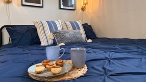 Ein Bett mit dunkelblauer Bettdecke, zwei Wandlampen und zwei gerahmte Blumenbilder.