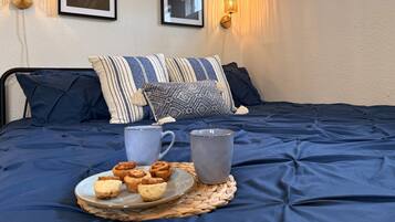 Un lit recouvert d’une couvre-lit bleu foncé, deux lampes fixées au mur et deux tableaux représentant des motifs floraux, encadrés.