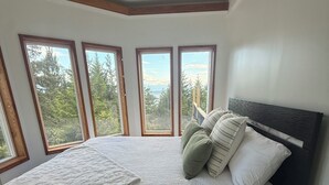 Een slaapkamer met een groot bed, meerdere ramen en uitzicht op bomen.