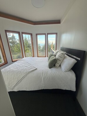 A bedroom with a large bed, multiple windows, and a view of trees. - Beautiful View, Pet Friendly, Rural, Luna Blanca Lookout  (Sooke)