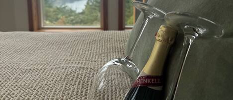 Una botella de vino HENKEll con una copa sobre un sofá texturizado, con vistas a zonas verdes y un edificio a través de una ventana.