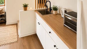 Een moderne keuken met een houten aanrecht, witte kastjes, een ingebouwde oven en een raam met uitzicht op groen.