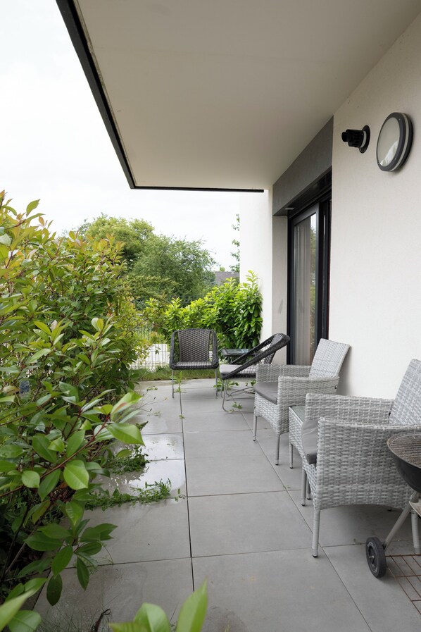 A patio with wicker furniture, a wheelbarrow, and a wall-mounted security camera. - Abracadabra Flat France Suisse near airport (Saint-Louis)