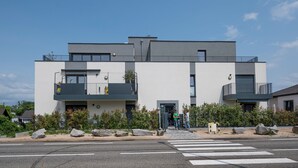 Moderni, kaksikerroksinen rakennus, jossa on parvekkeet, suojatie ja kirkas taivas.