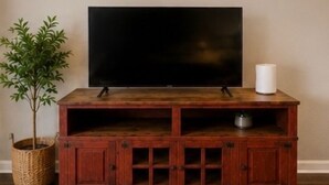 Un meuble de rangement en bois pour appareils multimédias, avec un téléviseur à écran plat, une bougie blanche et une plante en pot.