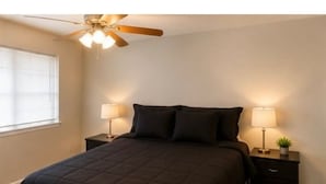 Une chambre à coucher avec un lit, deux tables de chevet avec des lampes, un ventilateur de plafond et une fenêtre.