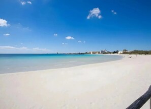 A beach with clear blue water, a sandy shore, and buildings in the background. - Eden Villa Privata Sul Mare (Porto Cesareo)