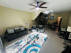 Un salon comprenant un canapé, deux fauteuils, un ventilateur, un ventilateur de plafond, un escalier et un coin repas.