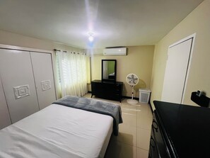 Une chambre d’hôtel avec deux lits, une commode, un miroir, un climatiseur, un ventilateur et une poubelle.