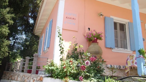 A building with a pink facade, blue shutters, and a sign that reads 'Agios Nikolaos.' - Aiolos Rooms (Tsoukalades)