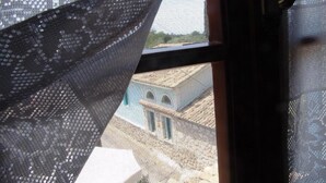 A window with a view of a building with a blue facade and arched windows. - Aiolos Rooms (Tsoukalades)