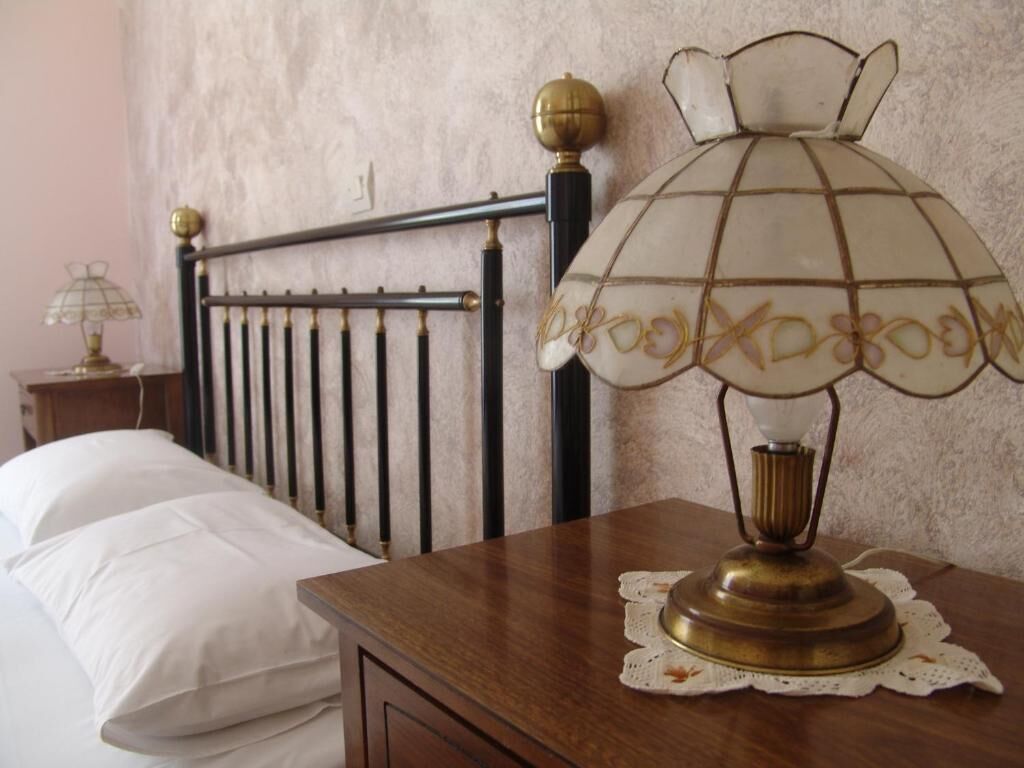 Een houten nachtkastje met een messing lamp, een wit bed met kussens en een hoofdbord met metalen frame.