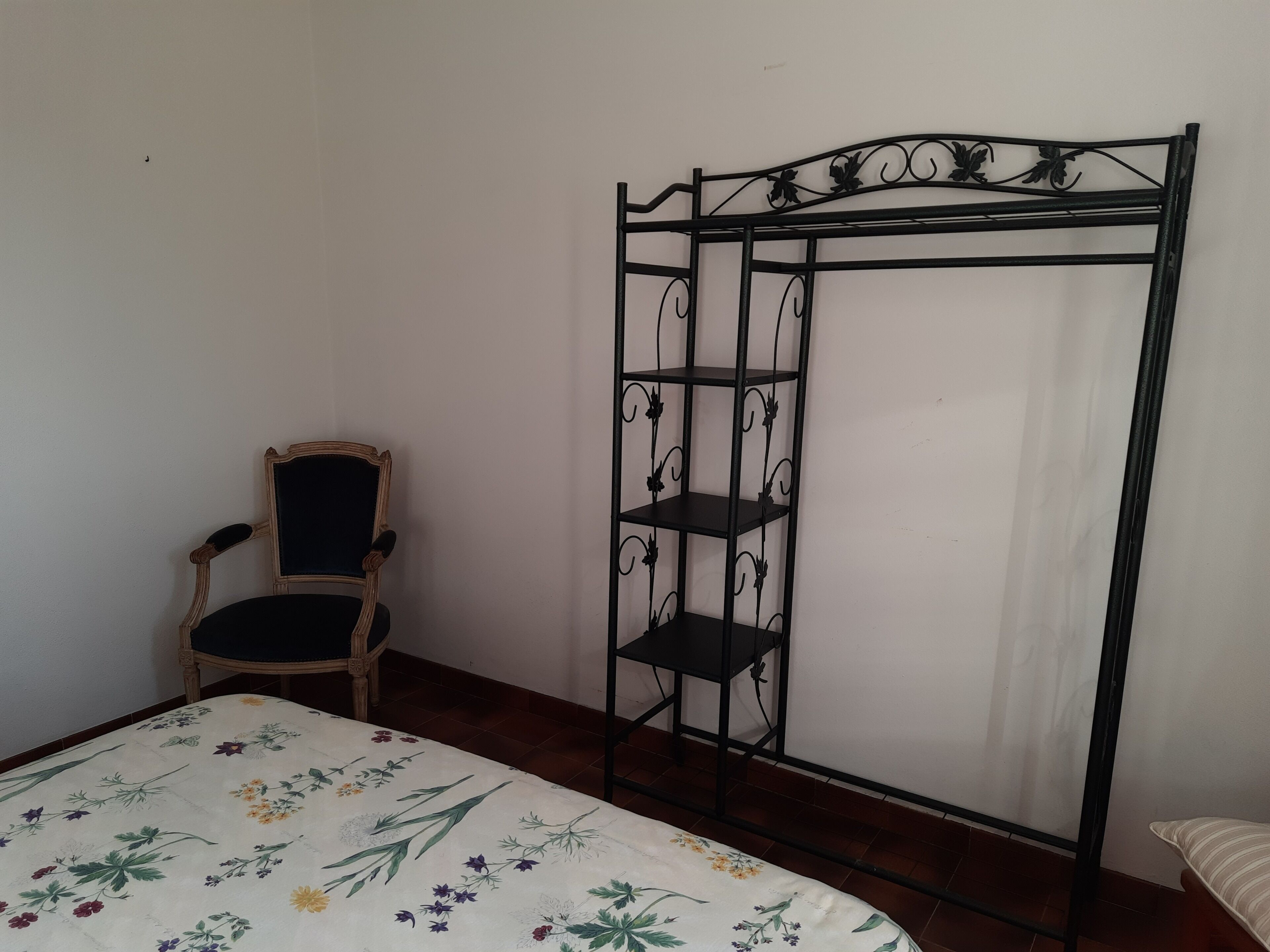 Un dormitorio con cama, una silla y un armario metálico con estantes.