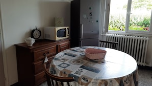 Una cocina con una mesa, sillas, microondas, refrigerador, un reloj y una ventana con vista a follaje.