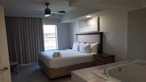 A hotel room with a bed, a ceiling fan, a window with curtains, a painting, a nightstand, and a bathtub. - Luxurious resort stay with amazing all-inclusive amenities near Orlando Florida! (Kissimmee)