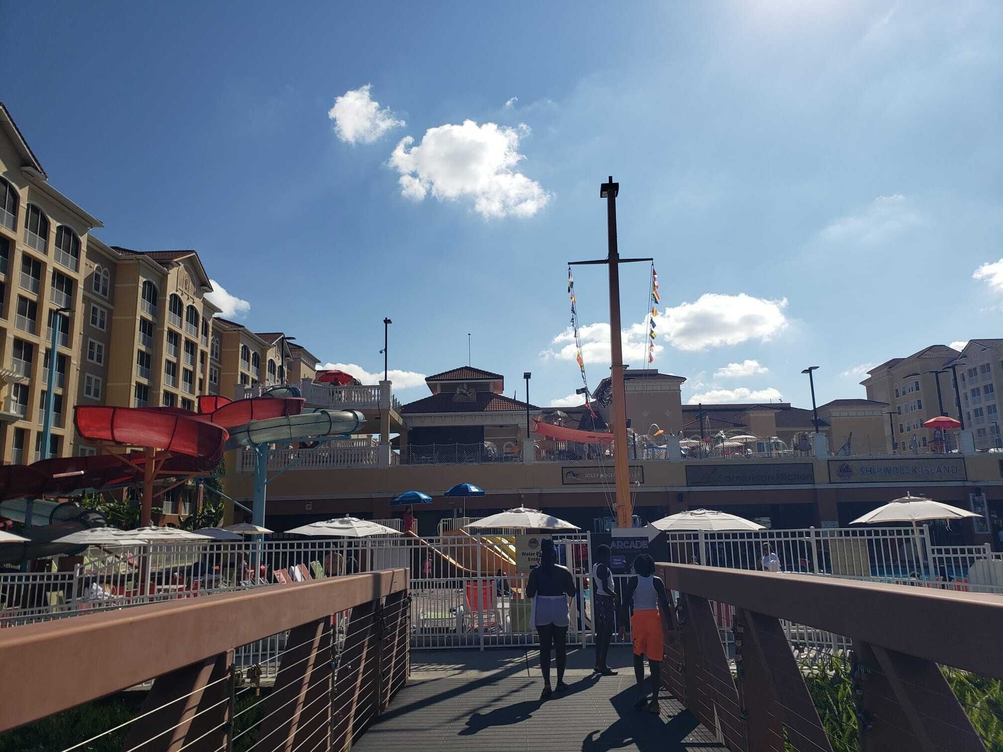 A boardwalk with a water slide, umbrellas, and buildings in the background.